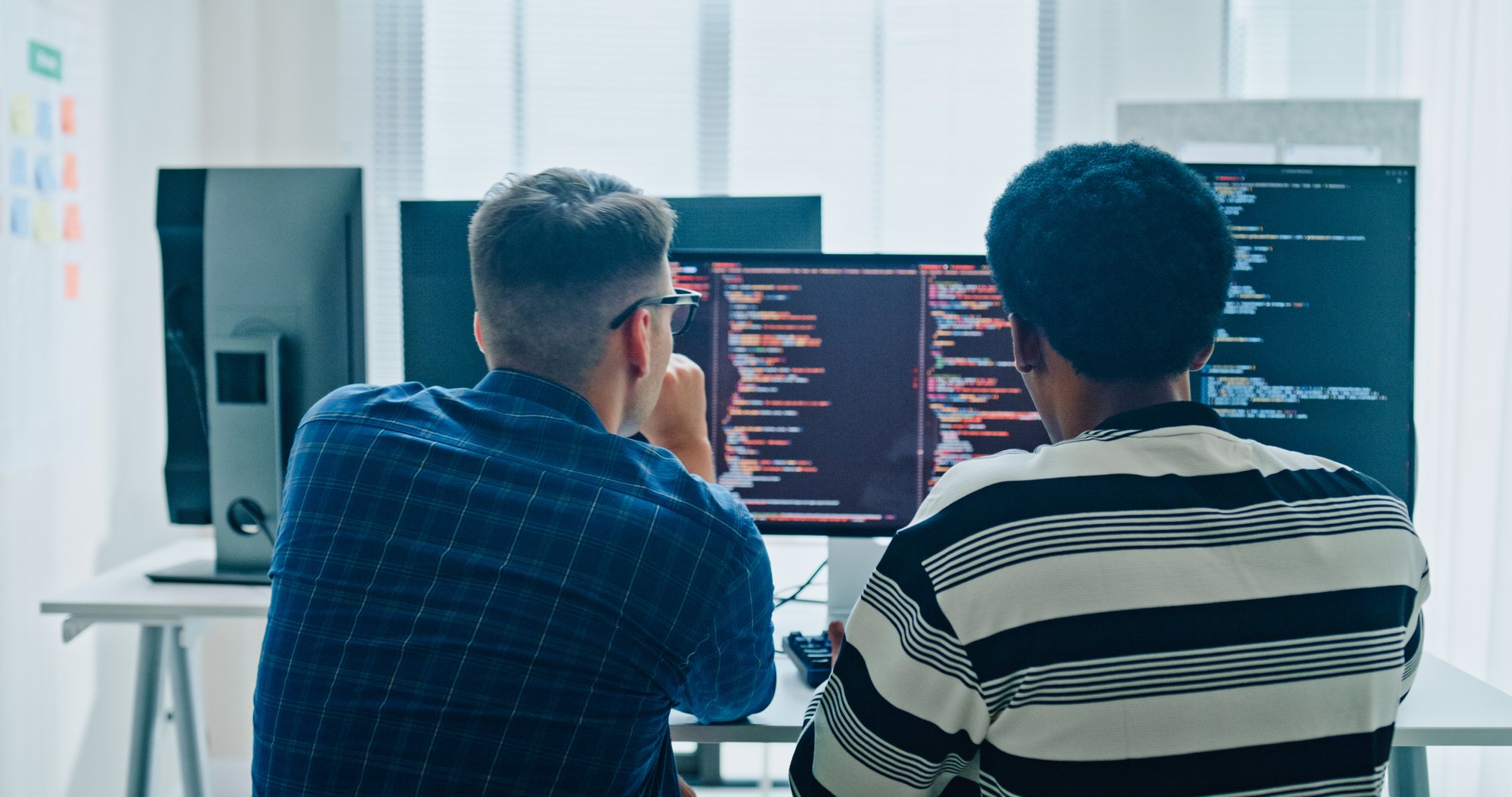 Two colleagues reviewing code together on dual monitors